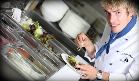 Koch in Kochjacke mit Schmidt-Buffetservice-Logo richtet einen Salatteller an