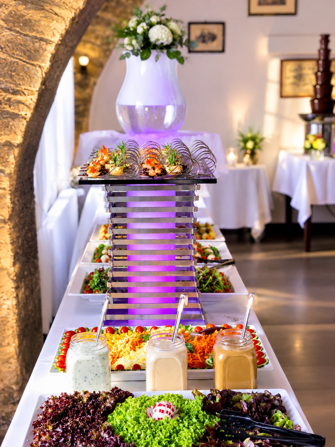 Salatbuffet mit beleuchteter Etagere und Blumendekoration unter einem Steinbogen